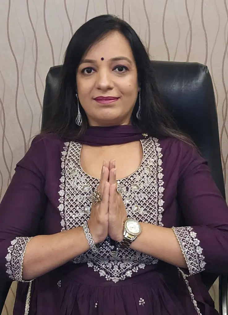Woman in a purple traditional outfit with silver embroidery sitting in a chair against a textured wall.